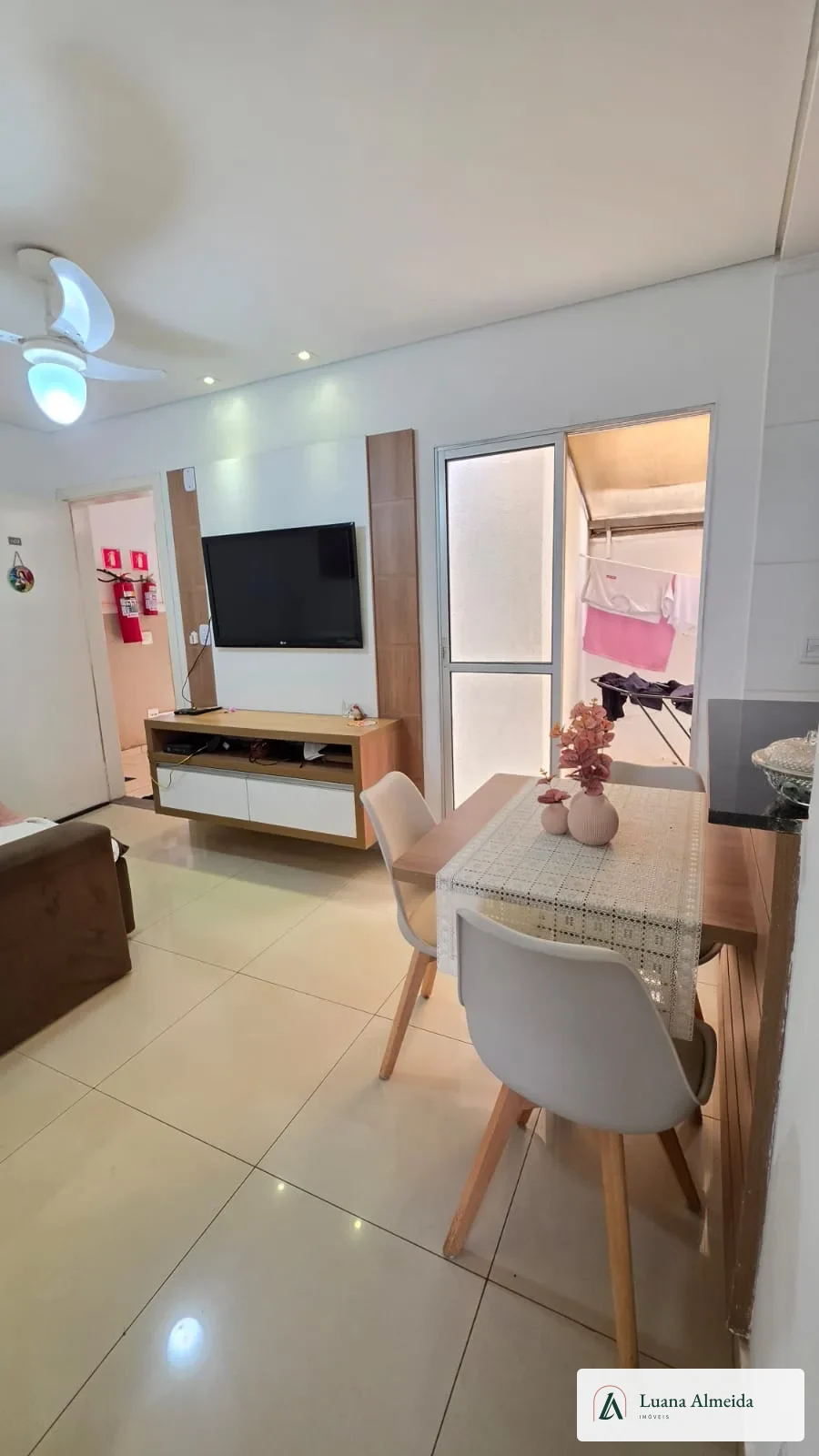 Sala integrada com painel de TV, mesa fixa com cadeiras e acesso ao quintal.