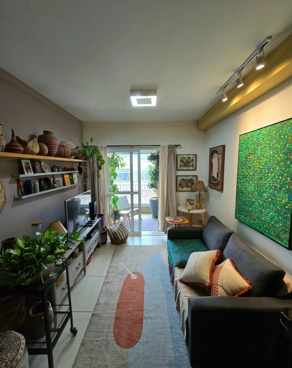 Sala de estar do apartamento com sofá, quadro verde e acesso à varanda; mobiliário fotografado.