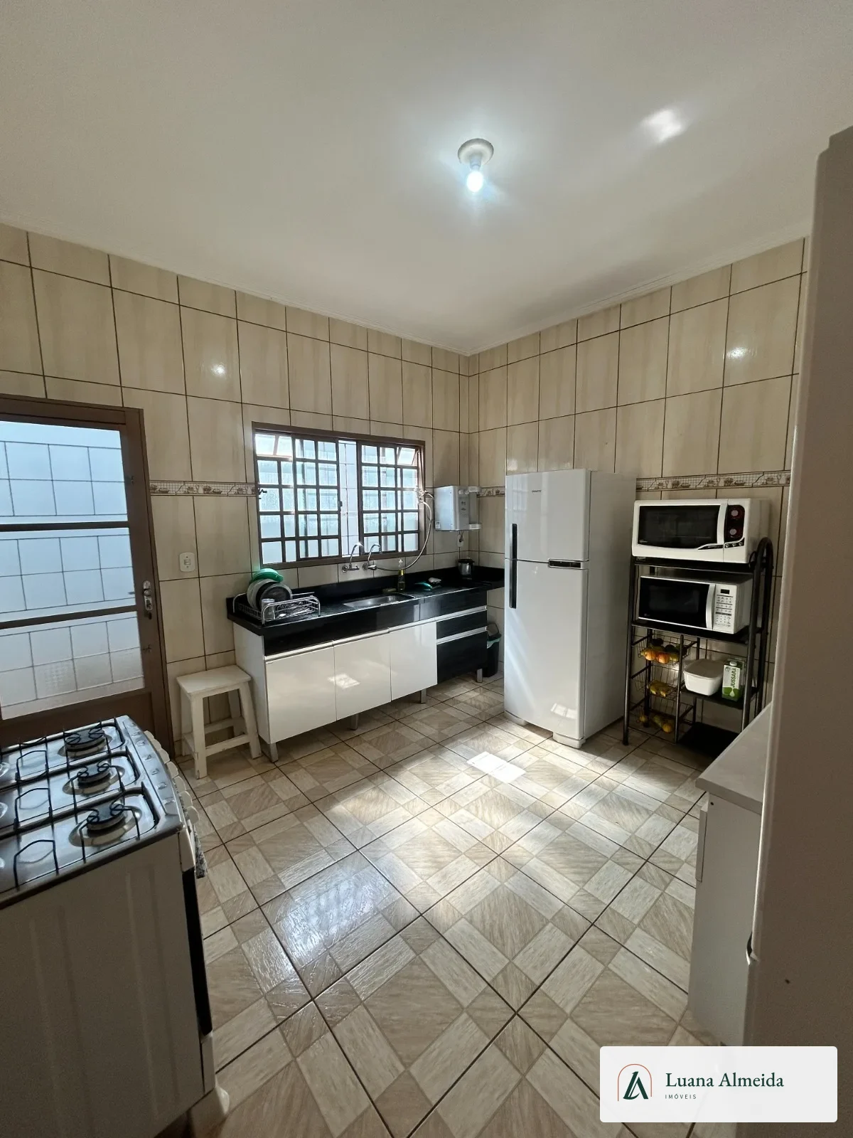 Cozinha da casa com bancada, armários, janela e eletrodomésticos fotografados.